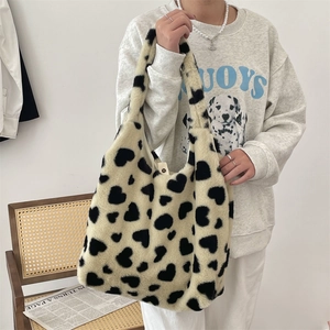 Detail of plush heart-patterned tote bag held by a model in a cozy winter setting