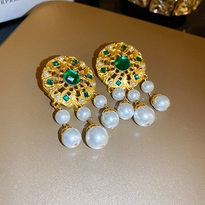 Close-up of vintage gold earrings with green gemstones and white pearl tassels