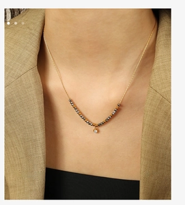 Detail of gold chain necklace with dark grey beads and clear zircon pendant on model
