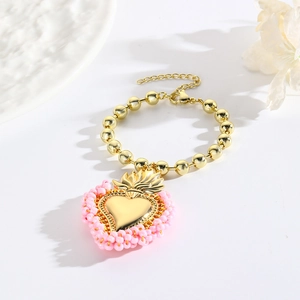 Makroaufnahme von Goldperlenarmband mit rosa umrandetem Herzanhänger und Karabinerverschluss