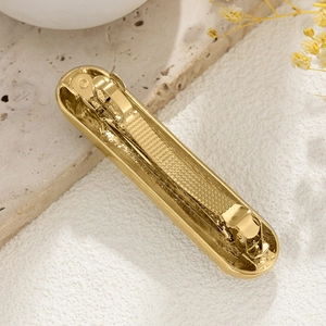 Detail of a retro gold curved metallic hair clip on a natural white marble background