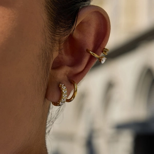 Détail de boucles d'oreilles cœur dorées et d'un ear cuff en cristal portés sur l'oreille