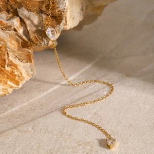 Elegant gold chain necklace featuring two teardrop rhinestones on a natural rock surface