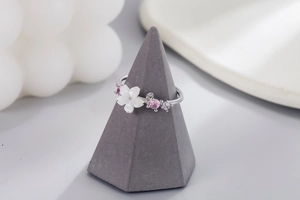 Detail of silver sakura ring with shell petals and pink zircons on jewelry stand