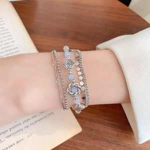 Detail of layered silver bracelet set with blue beads and vintage floral pendants on wrist