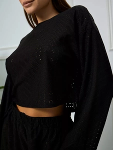 Dettaglio del crop top nero a maniche lunghe con tessuto in pizzo traforato e girocollo