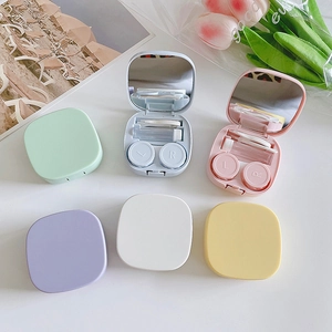 Flat lay of colorful portable contact lens cases with tweezers, mirror and solution bottle