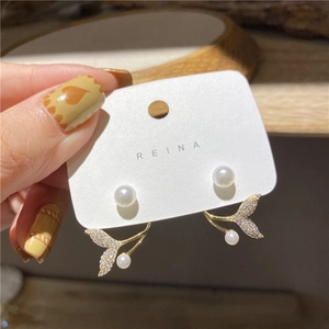 Detail of gold fish tail pearl earrings with micro-set zircon stones on display card