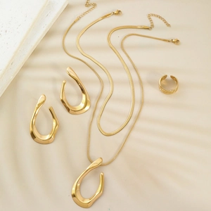 Golden stainless steel jewelry set featuring fluid necklaces, earrings and ring on stone