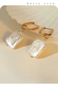 Detail of baroque pearl earrings with golden geometric hoops on shell background