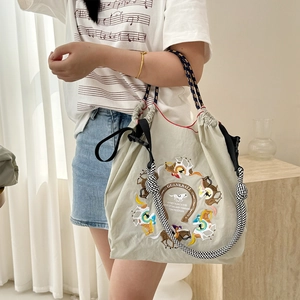 Detail of delicate colorful equestrian embroidery and woven rope handle on beige canvas bag