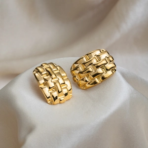 Boucles d'oreilles dorées géométriques tissées sur soie blanche avec texture élégante