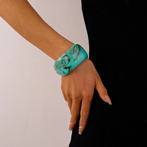 Detail of wide acrylic bangle with teal marble pattern on a model's wrist