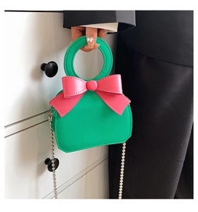 Detail of green handbag with pink bow decoration and elegant pearl chain handle