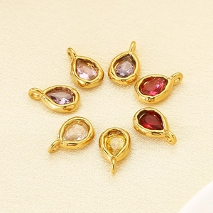 Set of seven gold-rimmed teardrop pendants with colorful faceted birthstones on beige fabric