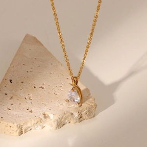 Close-up of teardrop zircon pendant on 18K gold plated chain resting on a natural stone