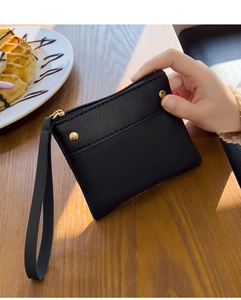 Close-up of black pebble leather coin purse with gold zipper and wrist strap on wooden table