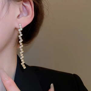 Close-up of elegant gold tassel earrings with zircon stones worn by a model in soft light