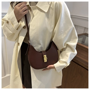 Detail of a dark brown leather crescent bag with gold buckle on a beige trench coat