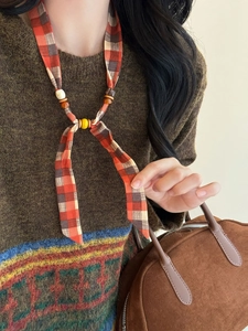 Close-up of ethnic plaid fabric necklace with wooden beads on brown knit sweater