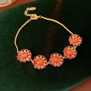 Macro shot of gold-plated bracelet with five red zircon floral charms on dark green velvet