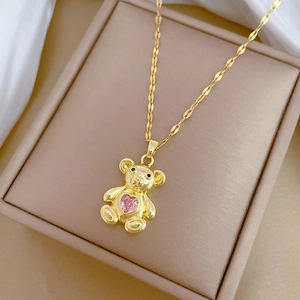 Close-up of golden teddy bear necklace with pink heart gemstone on white satin fabric