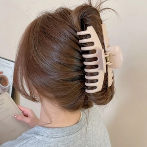 Close-up of a large beige matte hair claw clip holding a stylish bun in a soft setting