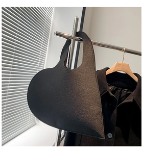Minimalist black heart-shaped felt handbag displayed on a sleek metal hanger
