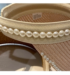 Close-up of pearl details on straw sun hat brim with inner label showing material info