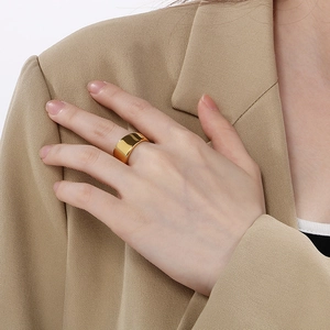 Close-up of a wide minimalist gold stainless steel ring worn with a beige suit