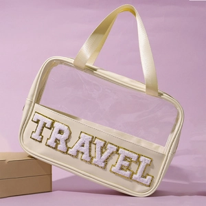 Detail of beige travel toiletry bag with clear PVC body and TRAVEL chenille patch