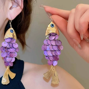 Detailed close-up of fish-shaped earrings with purple shimmering scales and gold accents