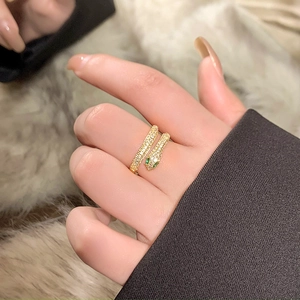 Detailed view of a gold snake ring with micro-pave crystals and green gemstone eyes