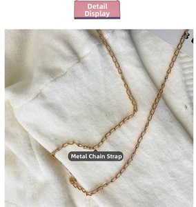 Detailed close-up of the golden metal chain strap on a white fuzzy plush handbag