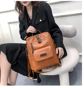 Close-up of tan PU leather backpack with multiple zipper pockets on a white stool
