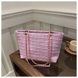 Detail of pink-purple textured tote bag with gold chain strap on wooden surface