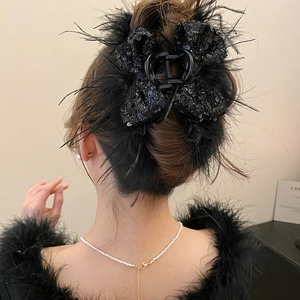Detail of a large black feather and sequin bow hair claw clip styled on a model's hair