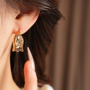 Macro shot of gold-plated U-shaped earrings with inlaid colorful mother-of-pearl flowers