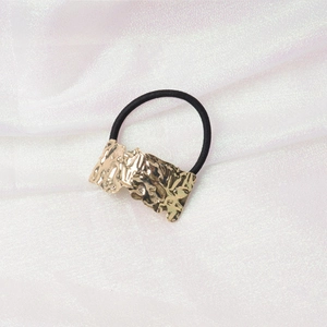 Detail of black elastic hair tie with textured gold metal accent on white silk fabric