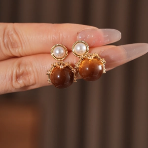 Close-up of golden earrings with white pearl and brown tiger eye stone beads