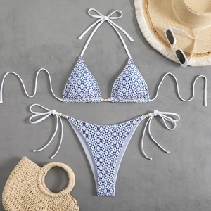 Two-piece halter bikini set with blue floral print and pearl detail on flat lay surface