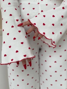 Detail of white ribbed knit pajama set featuring red heart print and lettuce edge cuffs