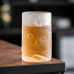 Cat and persimmon frosted glass tea cup with embossed pattern on wooden table