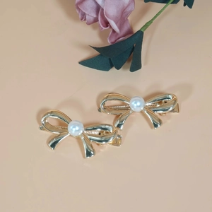 Pair of gold metal bow hair clips with white pearls on a minimalist beige background