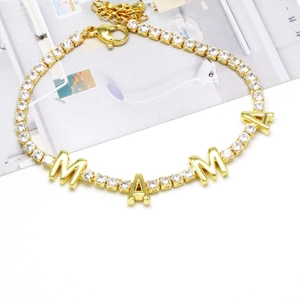 Detailed close-up of golden MAMA letter bracelet with clear zircon stones on white desk