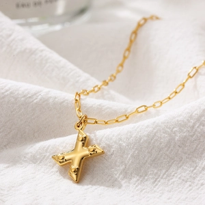 Detailed close-up of golden bubble letter X pendant necklace on white textured fabric