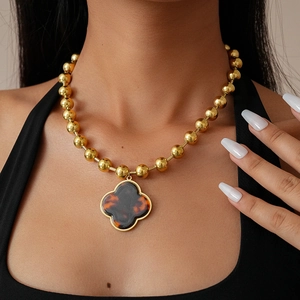 Detail view of gold beaded necklace with a tortoiseshell patterned clover pendant worn on model