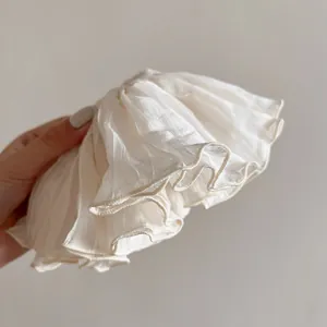 Detail of cream organza hair scrunchie with pleated texture shown held by hand
