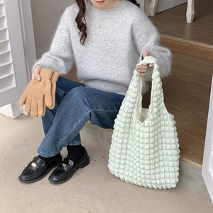 Detail of light green bubble textured shoulder bag paired with brown knitted gloves
