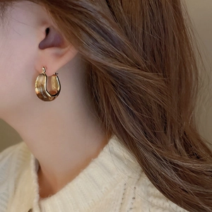 Close-up of golden U-shaped chunky hoop earring on a model with minimalist retro style
